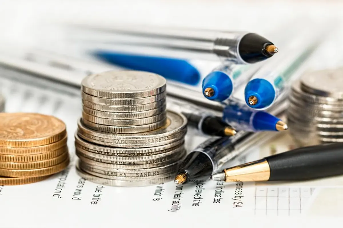 Monedas apiladas junto a documentos y bolígrafos